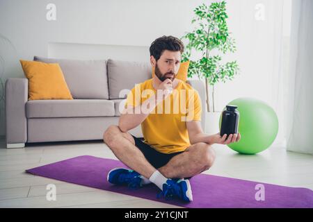 Photo de l'homme barbu athlétique attrayant dans la tenue de la main de vêtements de sport complément sportif pilules remède naturel à l'intérieur de la salle de gym à domicile Banque D'Images