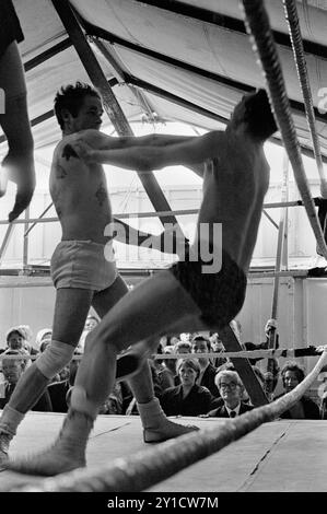 Tag Wrestling dans le spectacle de boxe Fairground Travellers de Pat McKeowen. Jack Turner (extrême gauche fumant dans le public) il a mené les combats au stand de boxe de Pat McKeowen. Epsom Downs, Surrey Angleterre juin 1969 1960 Royaume-Uni HOMER SYKES Banque D'Images