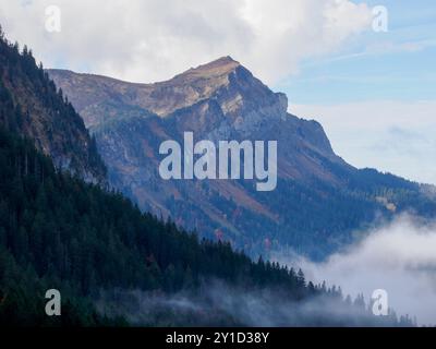 Un des sommets environnants du Mont Pilate, près de Lucerne en Suisse. La forêt et les nuages bas couvrent le premier plan, avec le pic illuminé. Banque D'Images