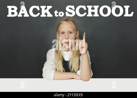 Petite écolière élève montrant l'inscription de retour à l'école sur fond de tableau noir. Concept d'éducation Banque D'Images