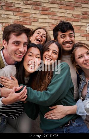 Groupe joyeux de jeunes amis divers appréciant de s'amuser avec le mur de briques Banque D'Images