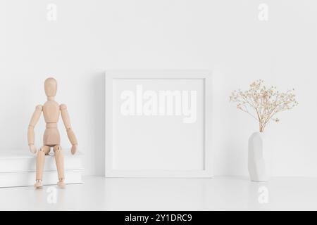 Maquette de cadre carré blanc avec des livres, mannequin et une gypsophile dans un vase sur une table blanche. Banque D'Images