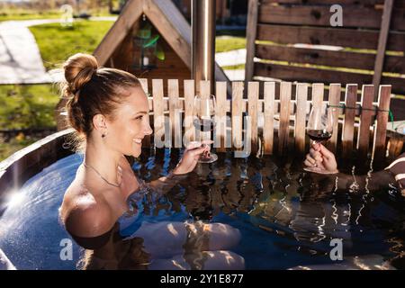 Jeune couple profitant dans le bain à remous extérieur, tremper dans l'eau chaude, entouré par la nature vierge, gros plan. Concept glamping et relaxation. Banque D'Images