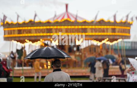 Attraction du parc d'expositions du carrousel à vapeur au sport automobile vintage immersif Goodwood Revival. Une journée grise et humide, des gens avec des parapluies noirs. Mise au point peu profonde. Banque D'Images