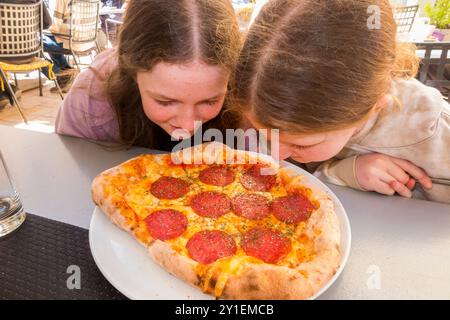 Soeurs, filles, enfants, enfant sentent fraîchement servi pizza au feu de bois à la table extérieure d'un restaurant Restoran Marko / Markos Pizzeria & Spaghetteria. Île de Hvar, Croatie. (138) Banque D'Images