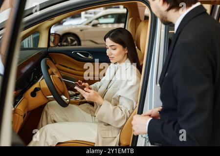 Jeune femme à la mode au siège des conducteurs lisant sur la performance de la voiture à l'aide de la tablette numérique tout en testant le véhicule de démonstration au centre de concession Banque D'Images