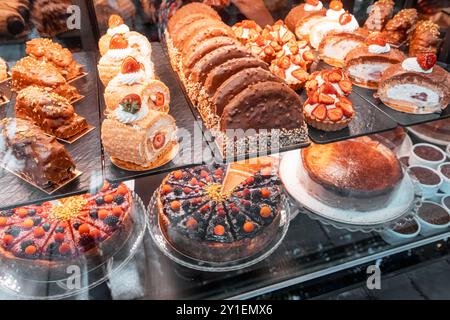 Une délicieuse exposition de gâteaux et pâtisseries assortis dans une vitrine de boulangerie, présentant une variété de desserts gastronomiques et de friandises sucrées Banque D'Images