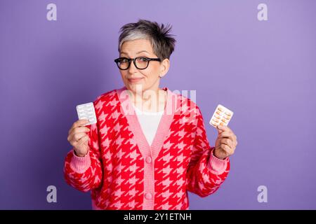 Portrait photo de jolie femme à la retraite tenir la thérapie de pilules porter la tenue rouge à la mode isolé sur fond de couleur violette Banque D'Images