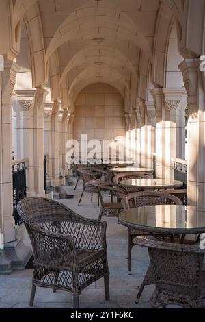 Un long couloir en pierre arqué avec une rangée de tables et de chaises aménagées pour les repas en plein air. La lumière du soleil traverse les arches. Banque D'Images