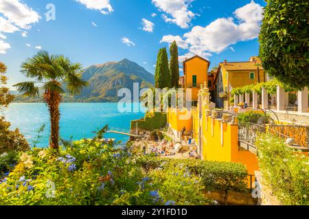 Bâtiments historiques, une petite plage et des palmiers dans le village de villégiature italien coloré de Varenna, en Italie, le long des rives du lac de Côme en été. Banque D'Images