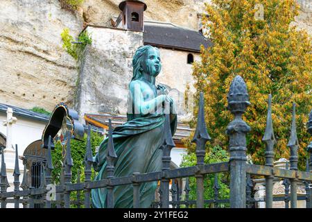 Statue en bronze d'une jeune fille comme pierre tombale commémorative sur une tombe dans le cimetière Saint-Pierre, avec l'ancienne abbaye catacombes derrière, Salzbourg Autriche Banque D'Images