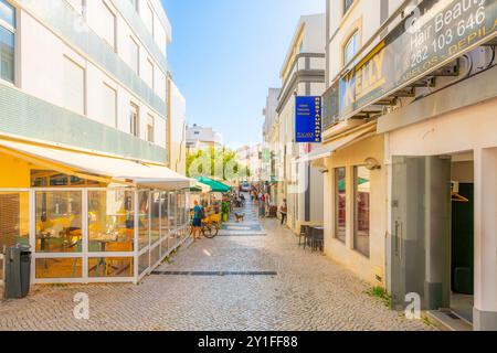 Une rue pittoresque à flanc de colline avec des cafés et des boutiques en trottoir dans la ville balnéaire blanchie à la chaux de Lagos, sur la côte de l'Algarve au Portugal. Banque D'Images