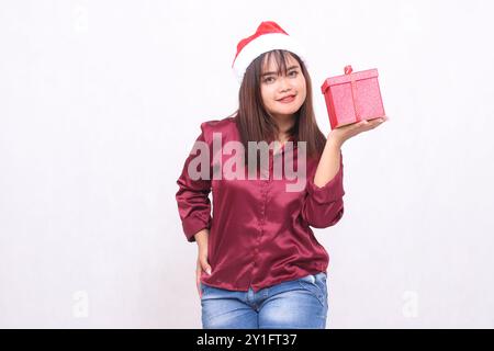 Portrait photo de belle fille asiatique embrassant âge portant boîte-cadeau dans noël chapeau de père noël moderne robe rouge brillant boîte de levage de main gauche Banque D'Images