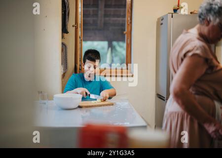 Jeune garçon préparant des légumes dans la cuisine avec grand-mère à proximité Banque D'Images