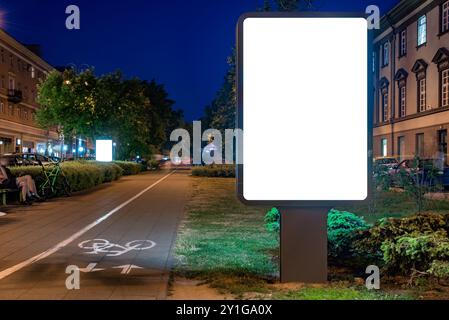 Blank White Billboard Mockup sur la rue piétonne à côté de la piste cyclable la nuit. Visionneuse pour affiches publicitaires pour la marque commerciale Banque D'Images