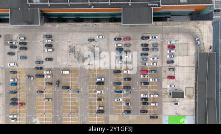 Vue aérienne d'un grand parking rempli de voitures variées, y compris des berlines et des VUS. Le lot montre un mélange de véhicules stationnés, avec quelques espaces vides Banque D'Images