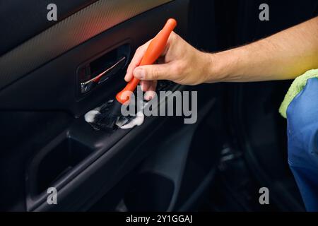 Homme nettoie toutes les surfaces dans la voiture avec une brosse Banque D'Images