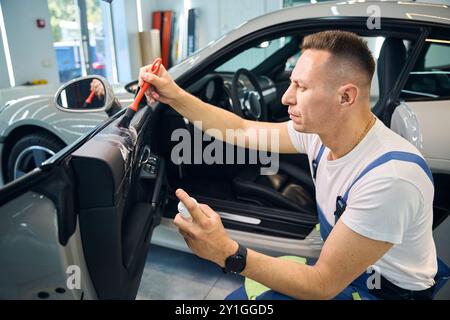 Un homme en salopette détaille une voiture Banque D'Images