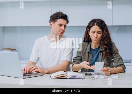 Un couple marié inquiet qui passe en revue les factures et gère les finances à la maison à l'aide d'un ordinateur portable et d'une calculatrice, en regardant les reçus du magasin, les reçus et les documents, est confronté à des problèmes de budgétisation. Banque D'Images