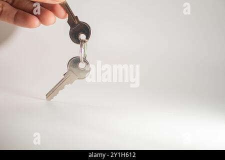 Une main tenant un jeu de clés avec un porte-clés sur un fond Uni. Les touches sont brillantes et métalliques, réfléchissant la lumière. Banque D'Images