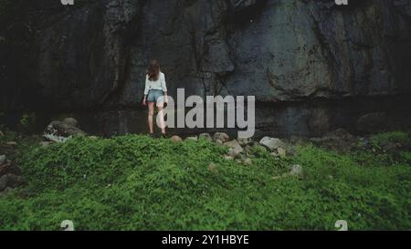 Jeune femme se tient dans la crainte de la nature, regardant une falaise rocheuse majestueuse sur une île tropicale. Ce paradis sauvage de polynésie française présente une jungle vierge de forêt tropicale et des panoramas pittoresques Banque D'Images