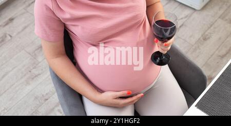 Une fille enceinte avec un gros ventre dans un chemisier rose tient un verre de vin. Le concept de boire de l'alcool pendant la grossesse, une mauvaise habitude. Banque D'Images