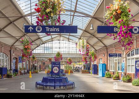 Le foyer d'une gare de chemin de fer renommée pour ses expositions florales. Des paniers suspendus pendent des chevrons et des sièges circulaires sont au centre. Banque D'Images