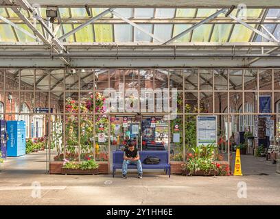 Le foyer d'une gare de chemin de fer renommée pour ses expositions florales. Des paniers suspendus pendent des chevrons et un passager est assis sur un banc. Banque D'Images