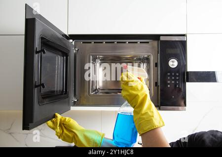 Spray anti-graisse dans la main d'une fille qui nettoie la cuisine. Nettoyer le four à micro-ondes de la graisse et de la saleté. Agent antistatique moderne. Banque D'Images