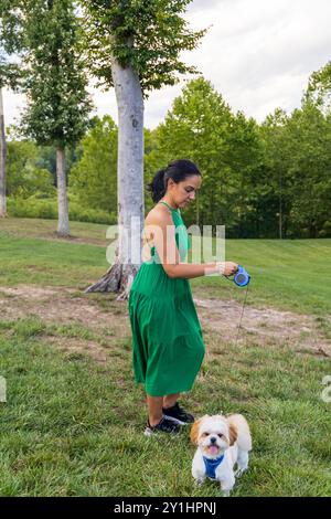 Une femme en robe verte promène son chien en laisse. Le chien est un petit caniche blanc. La scène est paisible et relaxante, avec la femme et son do Banque D'Images