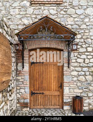 Une porte en bois robuste encadrée par un porte-à-faux de conception complexe, serrée contre un mur de pierre texturé. Des lanternes sont accrochées à côté de l'entrée dans une charmante atmosphère de village Banque D'Images