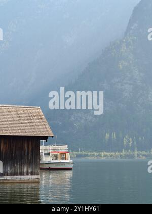 Hallstatt, Autriche - 31 août 2024 : une scène pittoresque avec un ferry traditionnel amarré à côté d'une maison rustique en bois sur un lac serein, encadré par t Banque D'Images