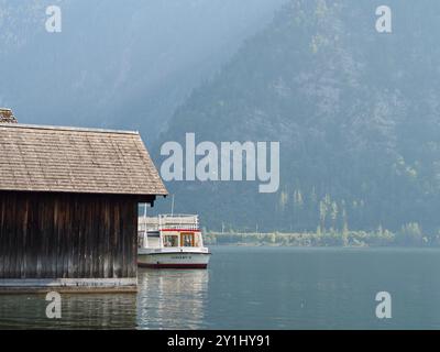 Hallstatt, Autriche - 31 août 2024 : une scène pittoresque avec un ferry traditionnel amarré à côté d'une maison rustique en bois sur un lac serein, encadré par t Banque D'Images