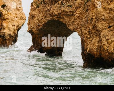Gros plan d'une arche côtière rocheuse sculptée par l'océan, avec des vagues qui coulent doucement à travers l'ouverture naturelle Banque D'Images