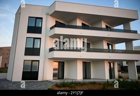 Immeuble moderne blanc avec balcons en verre reflétant le coucher du soleil. Banque D'Images