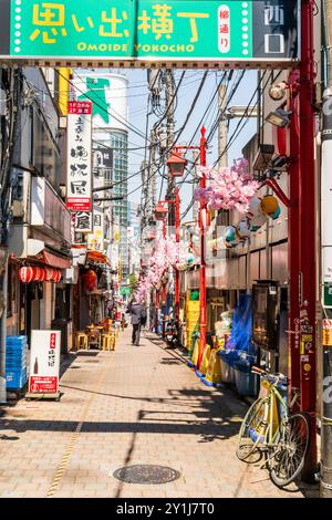 Salaryman marchant le long de Omoide Yokocho, une ruelle animée et nostalgique remplie de dîners traditionnels japonais izakaya et de nourriture de rue. Ciel bleu ensoleillé. Banque D'Images