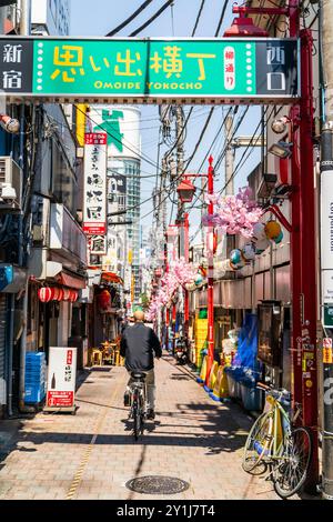 Homme à vélo le long de Omoide Yokocho, une ruelle animée et nostalgique remplie de dîners traditionnels japonais izakaya et de nourriture de rue. Ciel bleu ensoleillé. Banque D'Images