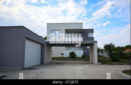 Maison de banlieue moderne et élégante avec garage et abri de voiture sur une journée ensoleillée avec un ciel bleu et des nuages blancs. Banque D'Images