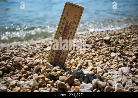 Thermomètre en bois indiquant le temps chaud de l'été sur une plage de galets avec la mer en arrière-plan. Banque D'Images