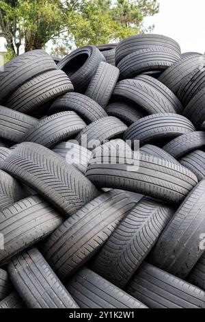 Une grande pile de pneus de voiture usagés en attente d'être recyclés, avec un arbre en arrière-plan. Banque D'Images