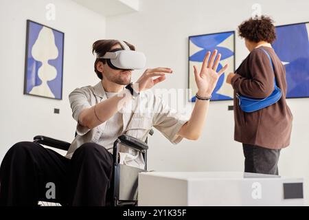 Portrait de vue latérale de l'homme handicapé en fauteuil roulant et portant la technologie VR tout en interagissant avec des œuvres d'art invisibles dans un espace de copie d'exposition d'art moderne accessible Banque D'Images