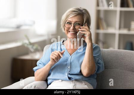 Femme plus âgée assise confortablement sur le canapé, engagée dans une conversation téléphonique Banque D'Images