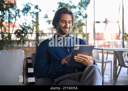 Heureux jeune homme d'affaires utilisant la tablette numérique assis à l'extérieur du bureau. Banque D'Images