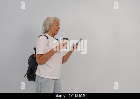 Une femme âgée profitant joyeusement de son café tout en envoyant des SMS sur son téléphone pendant la journée Banque D'Images