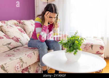 Adolescente malheureuse regardant le test de grossesse, bouleversée par le résultat, adolescent réfléchi stressé touchant le front, assis sur le canapé. Grossesse non désirée ou h Banque D'Images