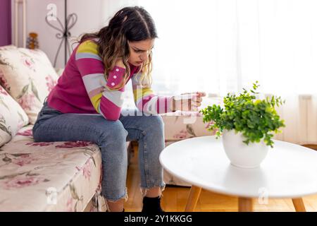 Adolescente frustrée assise sur le canapé regarder le test de résultat de grossesse négatif. Déçu adolescent stressé inquiet de grossesse non planifiée, fertili Banque D'Images