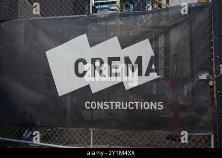 Bannière en maille noire et blanche Crema constructions, avec logo de la société, sur une porte de maillons de chaîne à l'extérieur d'un chantier de construction Banque D'Images