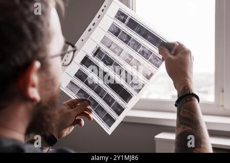 Photographe examinant des négatifs de film à la lumière de la fenêtre Banque D'Images