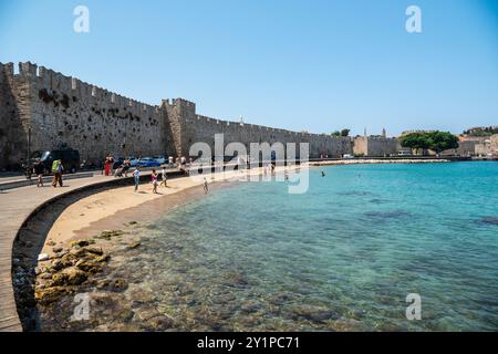 Rhodes Town, Grèce – 18 juillet 2024. Akti Sachtouri plage de sable dans la ville de Rhodes. Vue avec les murs de la vieille ville et les gens. Banque D'Images