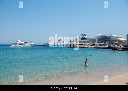 Rhodes Town, Grèce – 18 juillet 2024. Akti Sachtouri plage de sable dans la ville de Rhodes. Vue avec bateaux de croisière et terminal de croisière en arrière-plan. Banque D'Images